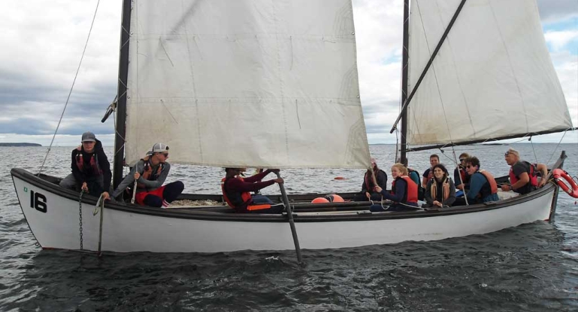 A group of students navigate a sailboat with white sails. 